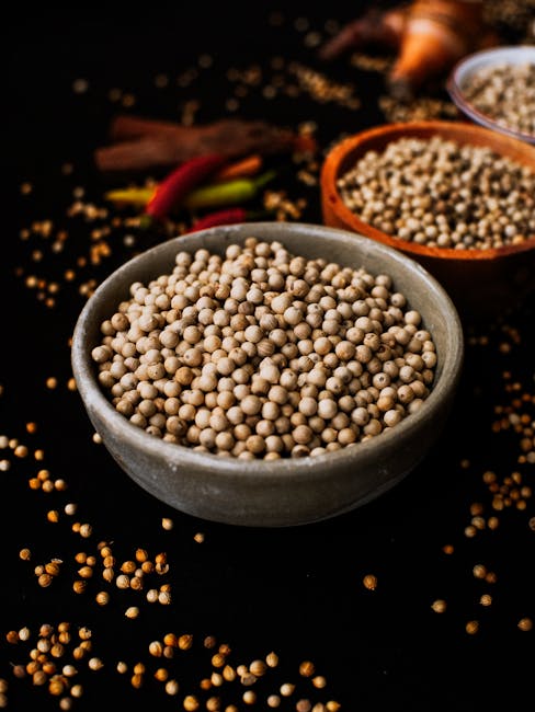 Close-up shot of white peppercorns in a ceramic bowl with scattered spices on dark background.