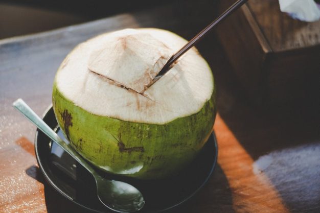 A close-up of a fresh coconut with a straw and spoon, beautifully captured indoors.